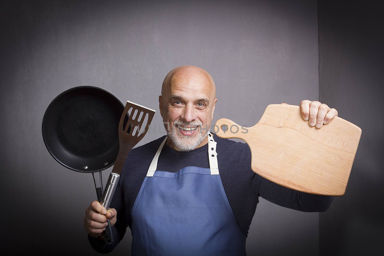 Gray-haired man with kitchen equipment on gray background
