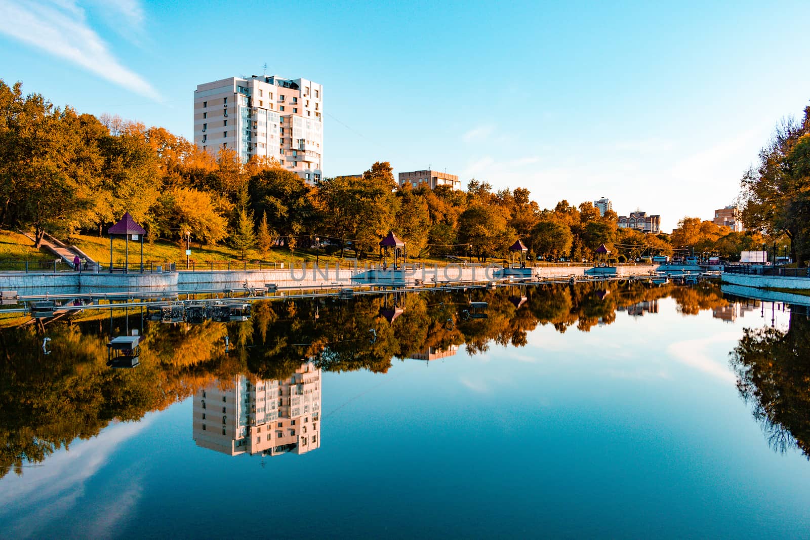 City ponds in the autumn. Trees covered with yellow and orange leaves are reflected in the water. Blue sky.