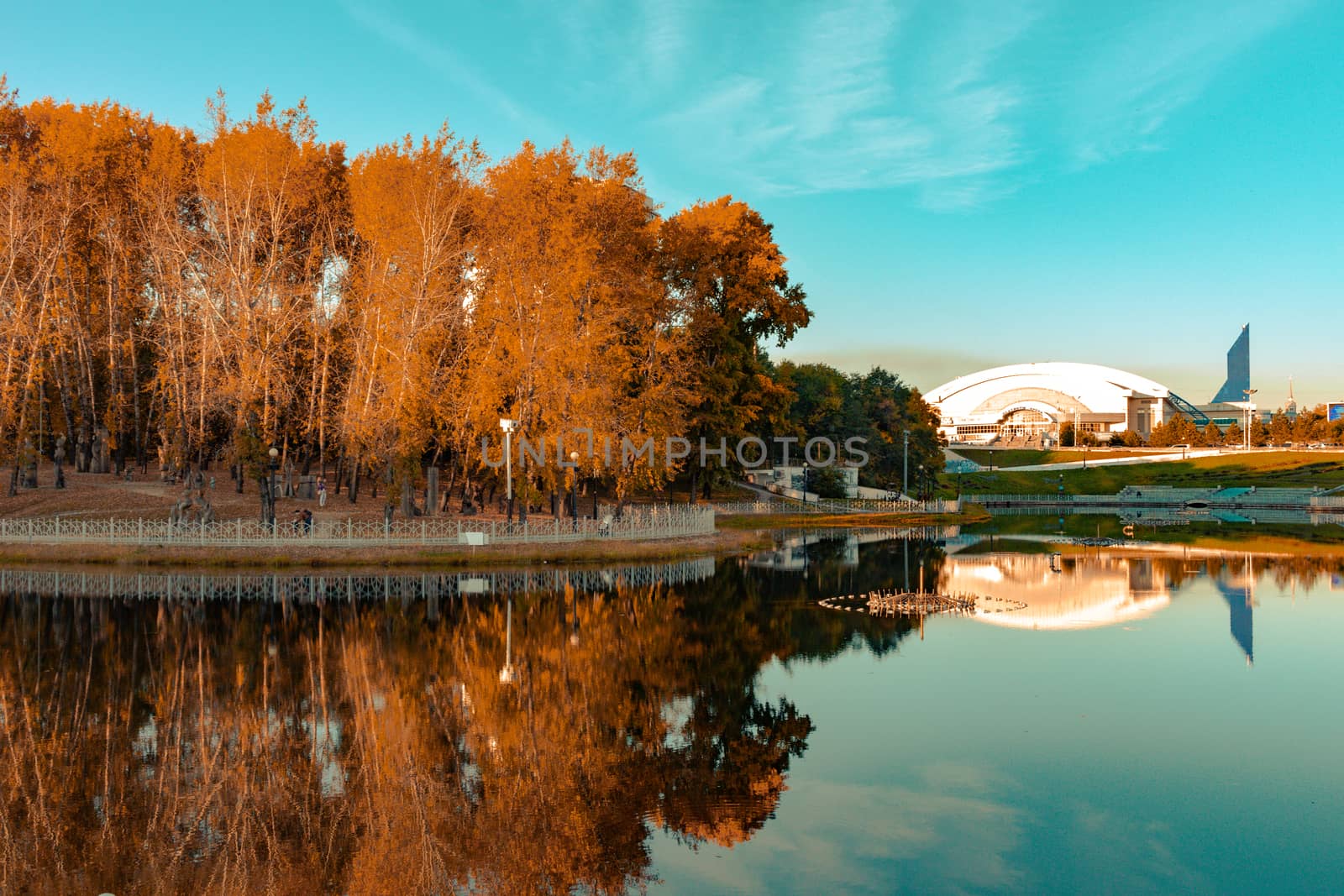 City ponds in the autumn. Trees covered with yellow and orange leaves are reflected in the water. Blue sky.