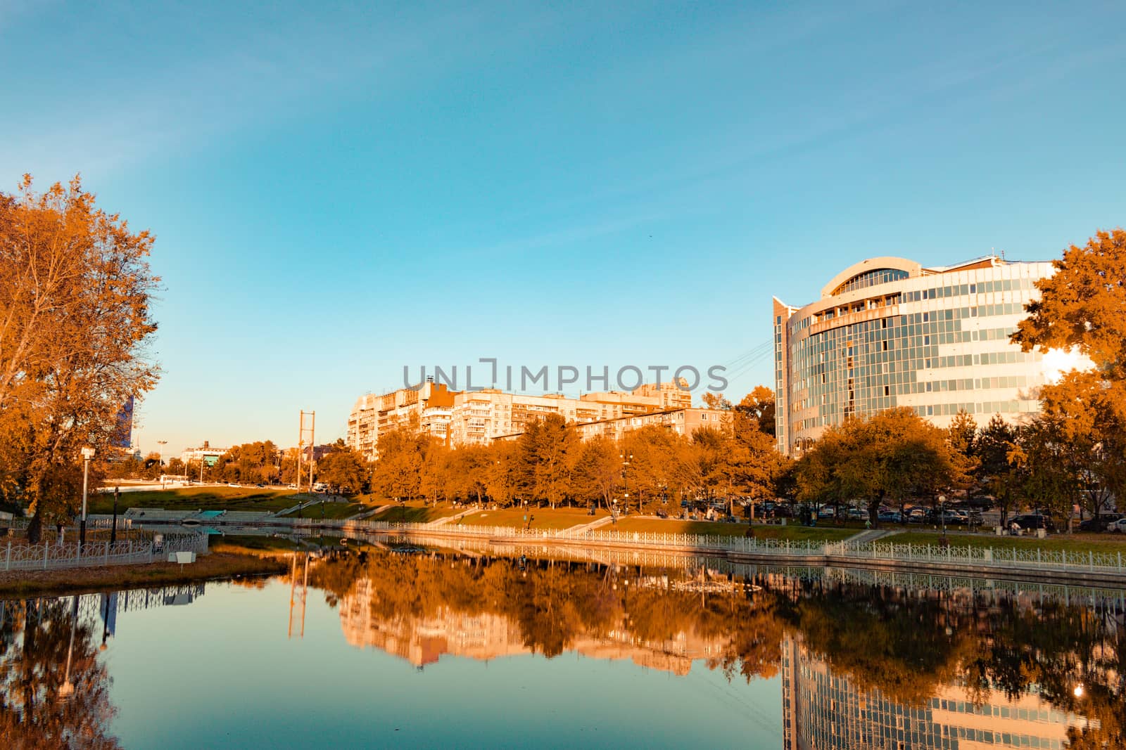 City ponds in the autumn. Trees covered with yellow and orange leaves are reflected in the water. Blue sky.