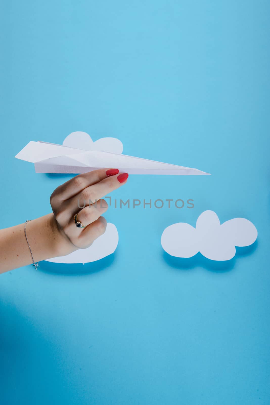 Paper plane in female hand on a blue background with clouds