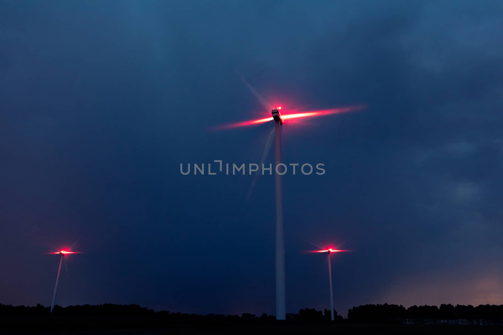 Wind turbines on a dramatic dark blue clouds in the sky. Storm ahead is coming. Red warning light on the windmill