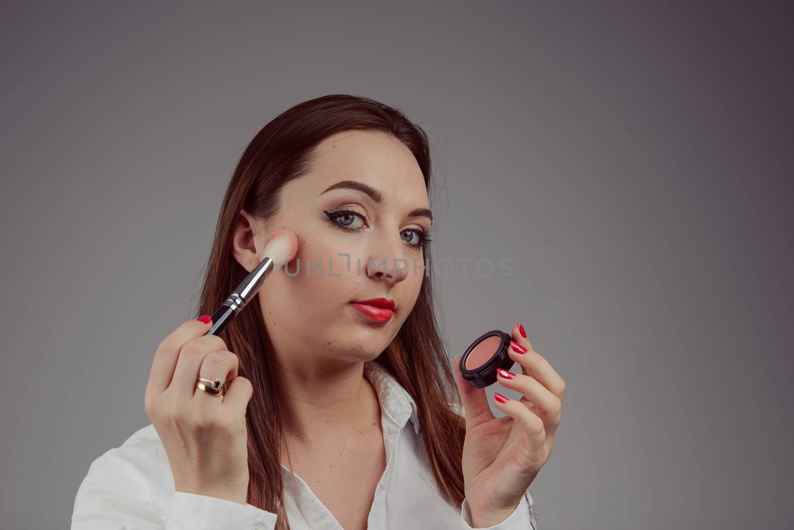 Beauty model teenage girl looking in the mirror and applying mascara make up. Beautiful young woman apply makeup by Brejeq