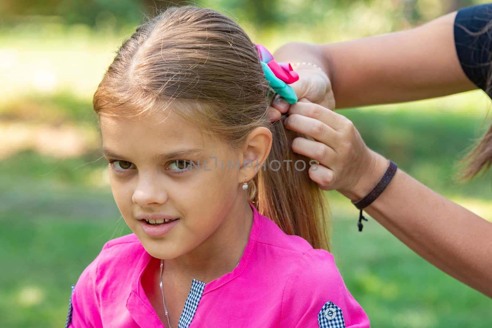 A teenager girl is tied a bow on long hair, on a picnic, close-up