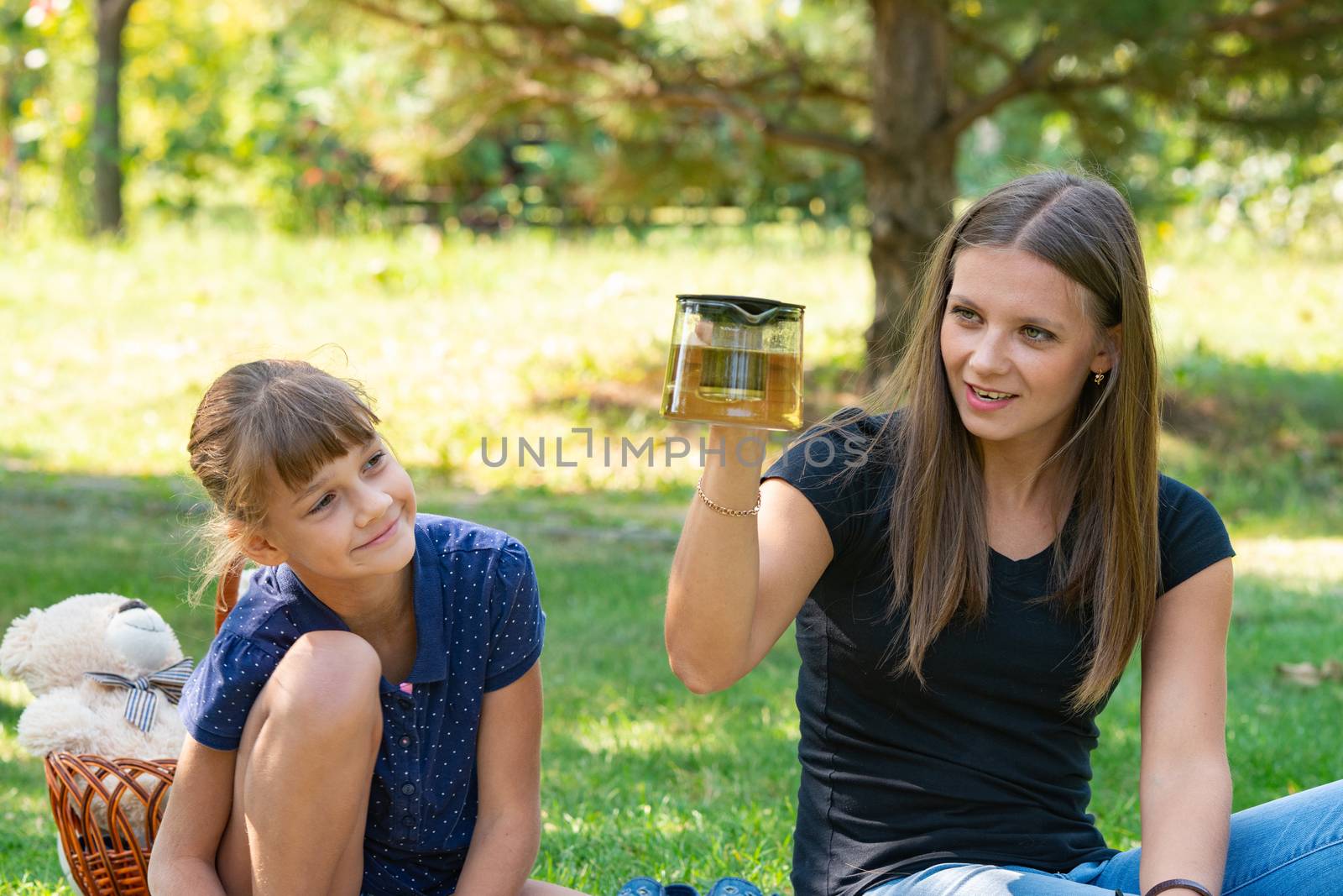 Girl and girl have fun at a teapot at a picnic