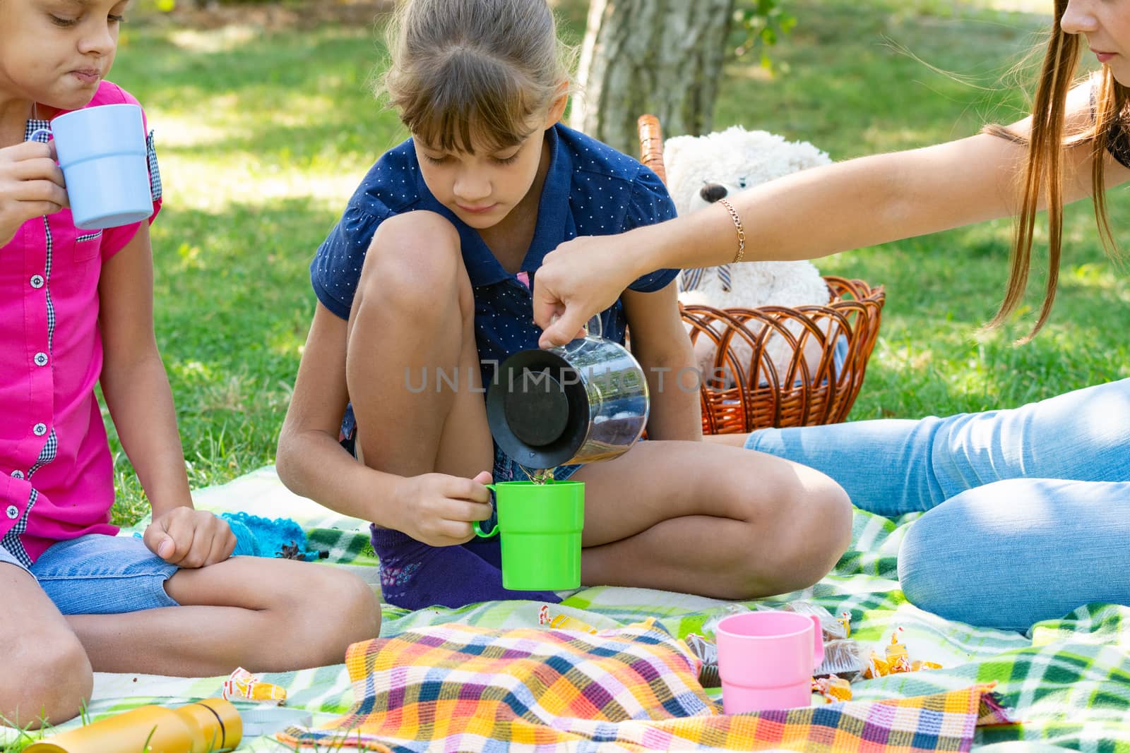 At a picnic, a girl pours tea in glasses for children