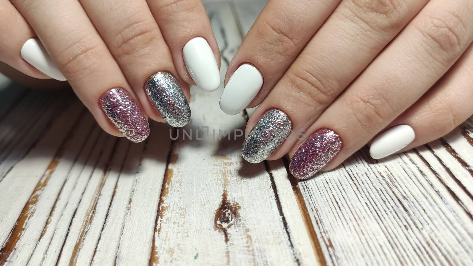 Closeup of hands of a young woman with dark red manicure on nails against white background