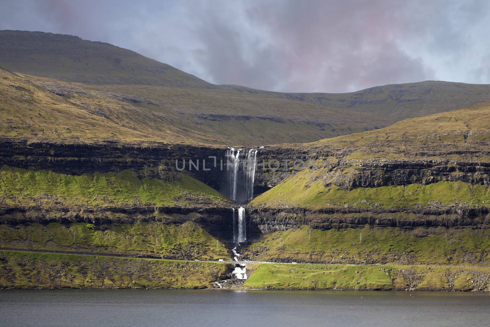 Spectacular mountain stream splashes over the rocky cliff, creating a breathtaking Fossa waterfall in rural parts of Faroe Islands