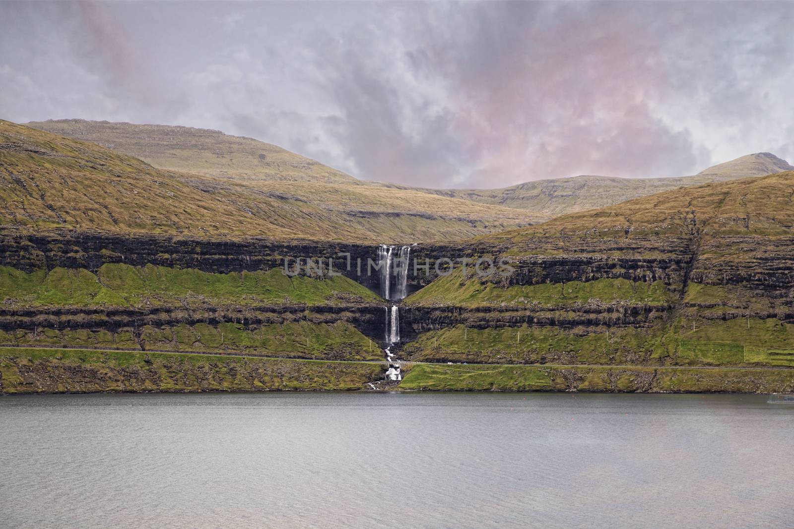 Spectacular mountain stream splashes over the rocky cliff, creating a breathtaking Fossa waterfall in rural parts of Faroe Islands