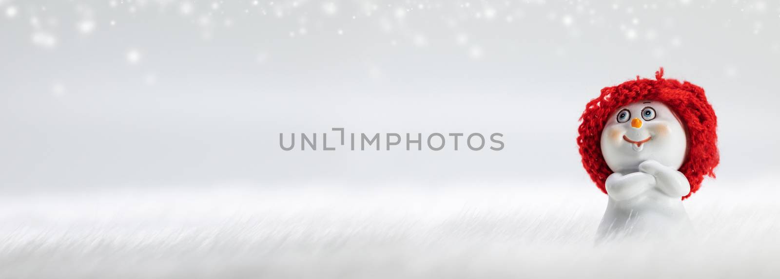 Snowman toy on frozen snow and bokeh lights winter background