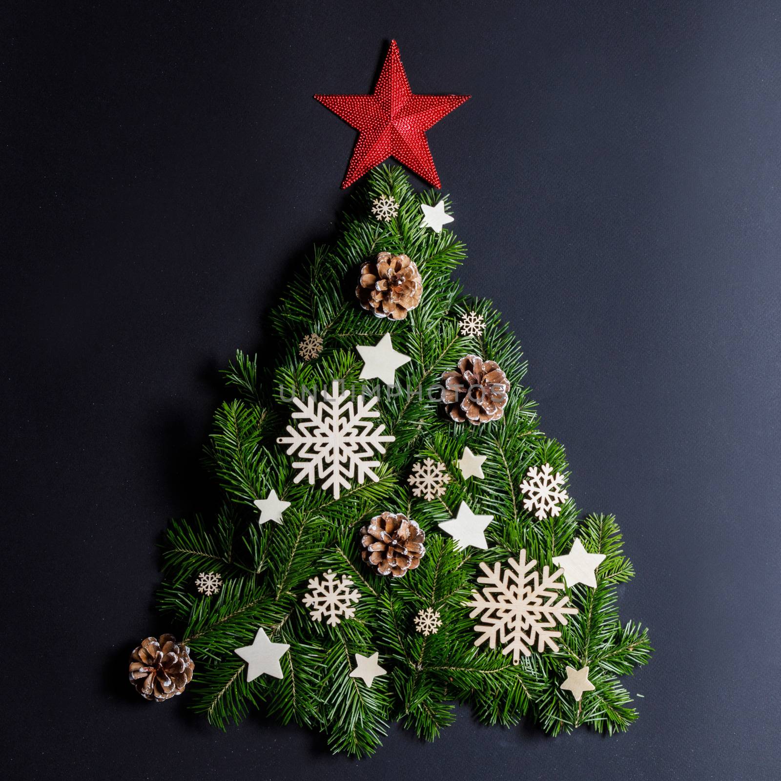 Christmas tree made of natural spruce branches deecor with red star on black background, flat lay card with copy space
