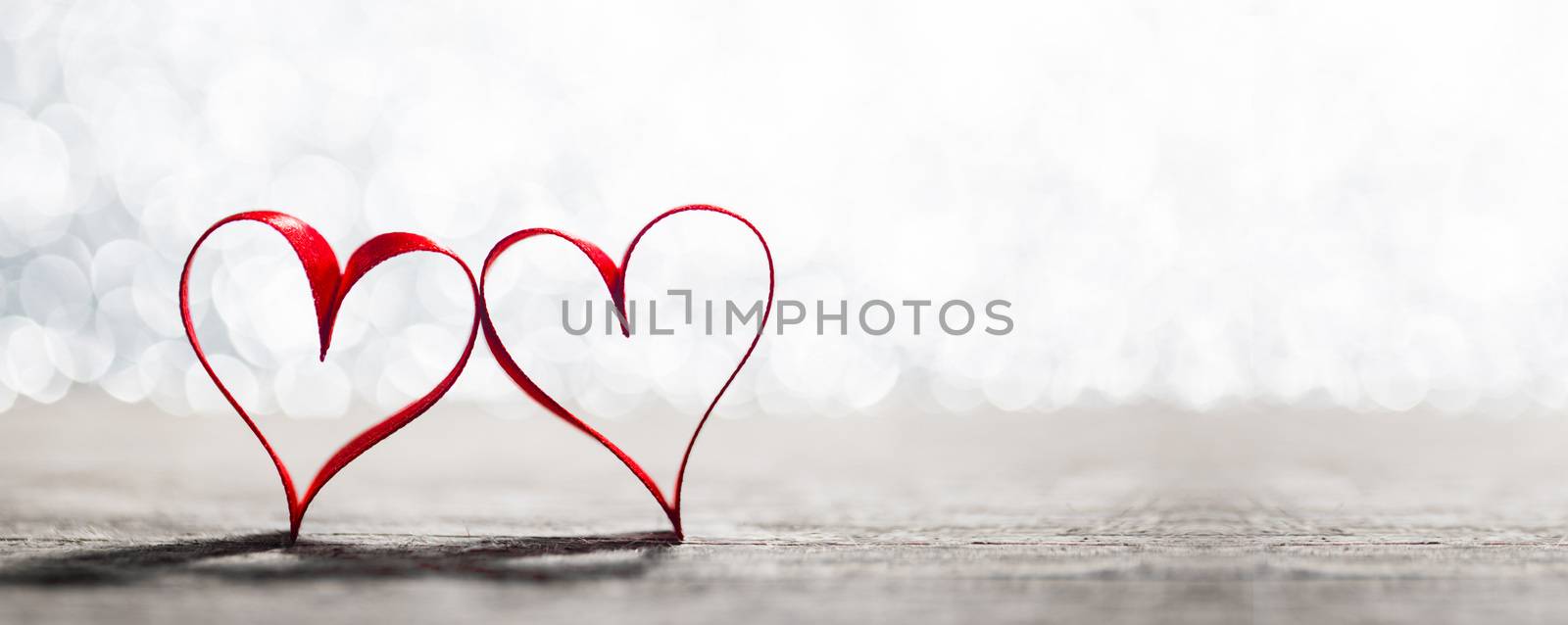 Two red ribbon hearts symbol of love on wooden background with beautiful bokeh, Saint Valentine Day celebration, copy space for text