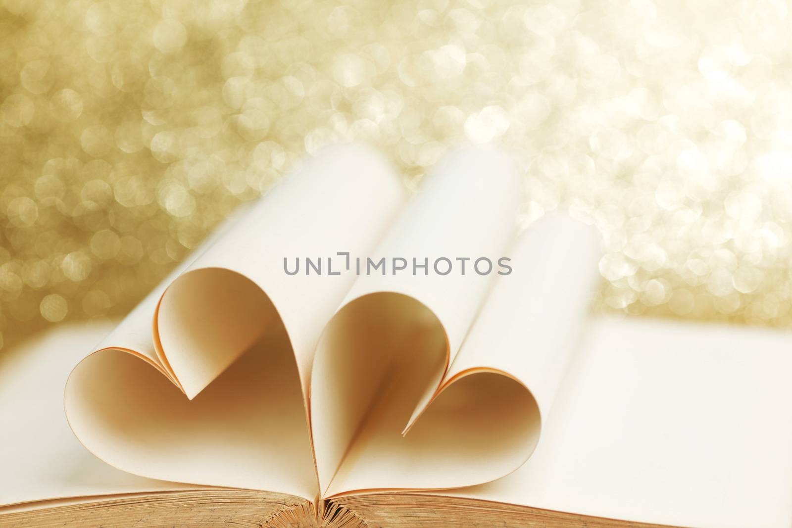 Pages of open book rolled in heart shape on glitter background