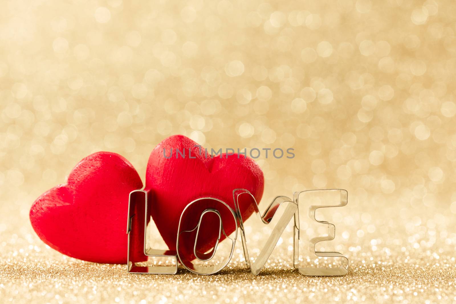 Two red handmade wooden hearts and word love on golden bright glitter lights bokeh background