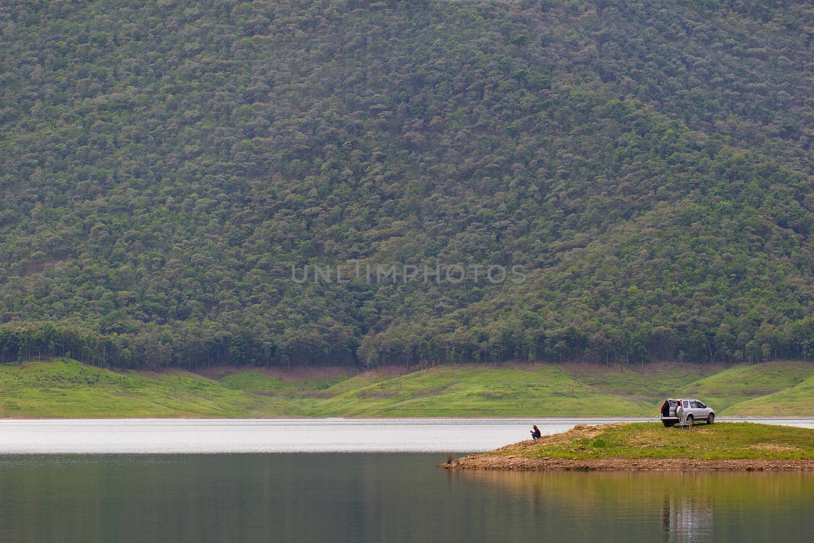 Men sitting and fishing on island at the dam. by SaitanSainam