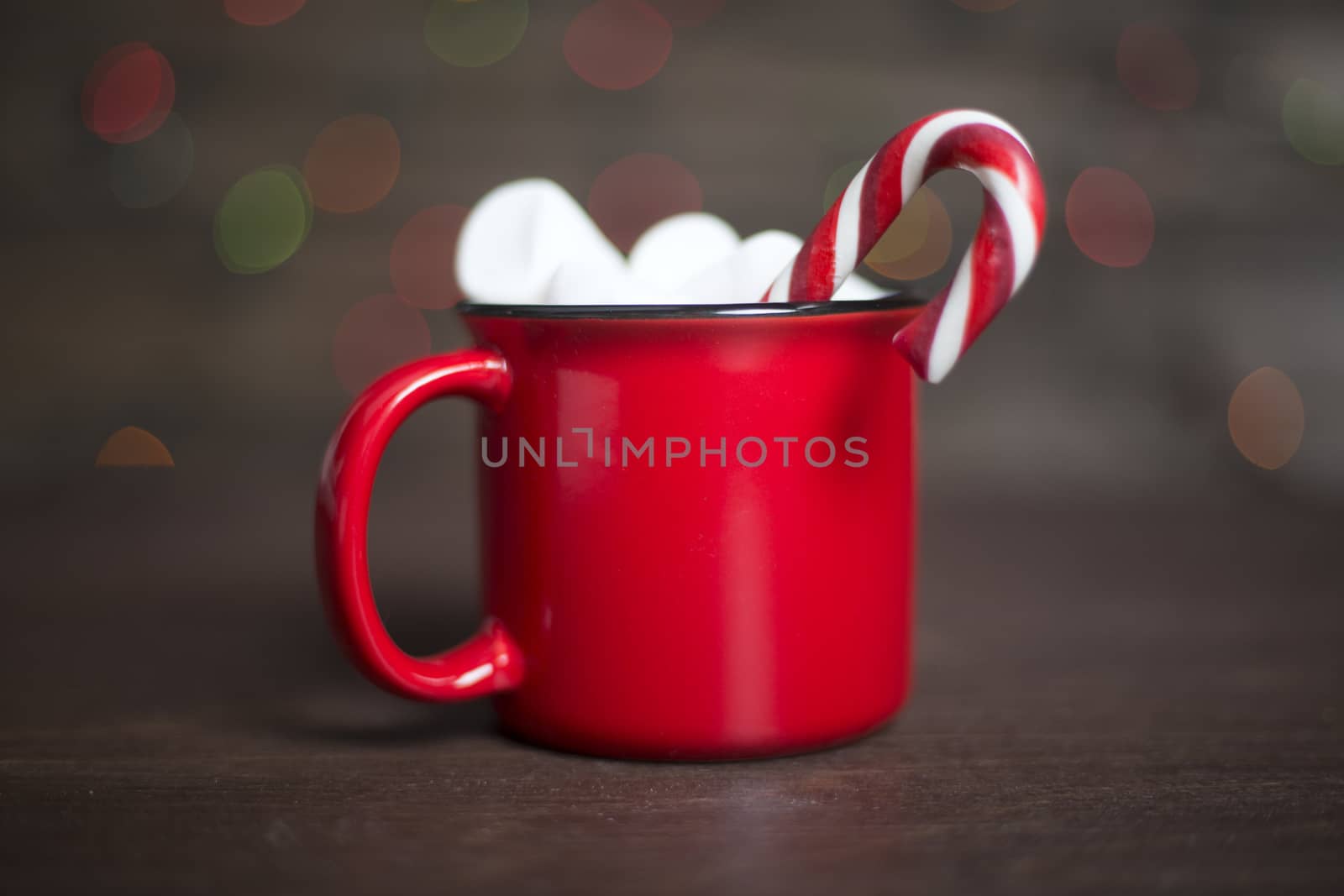 Cocoa in red mug with marshmallows and candy cane on dark wooden background with bokeh lights