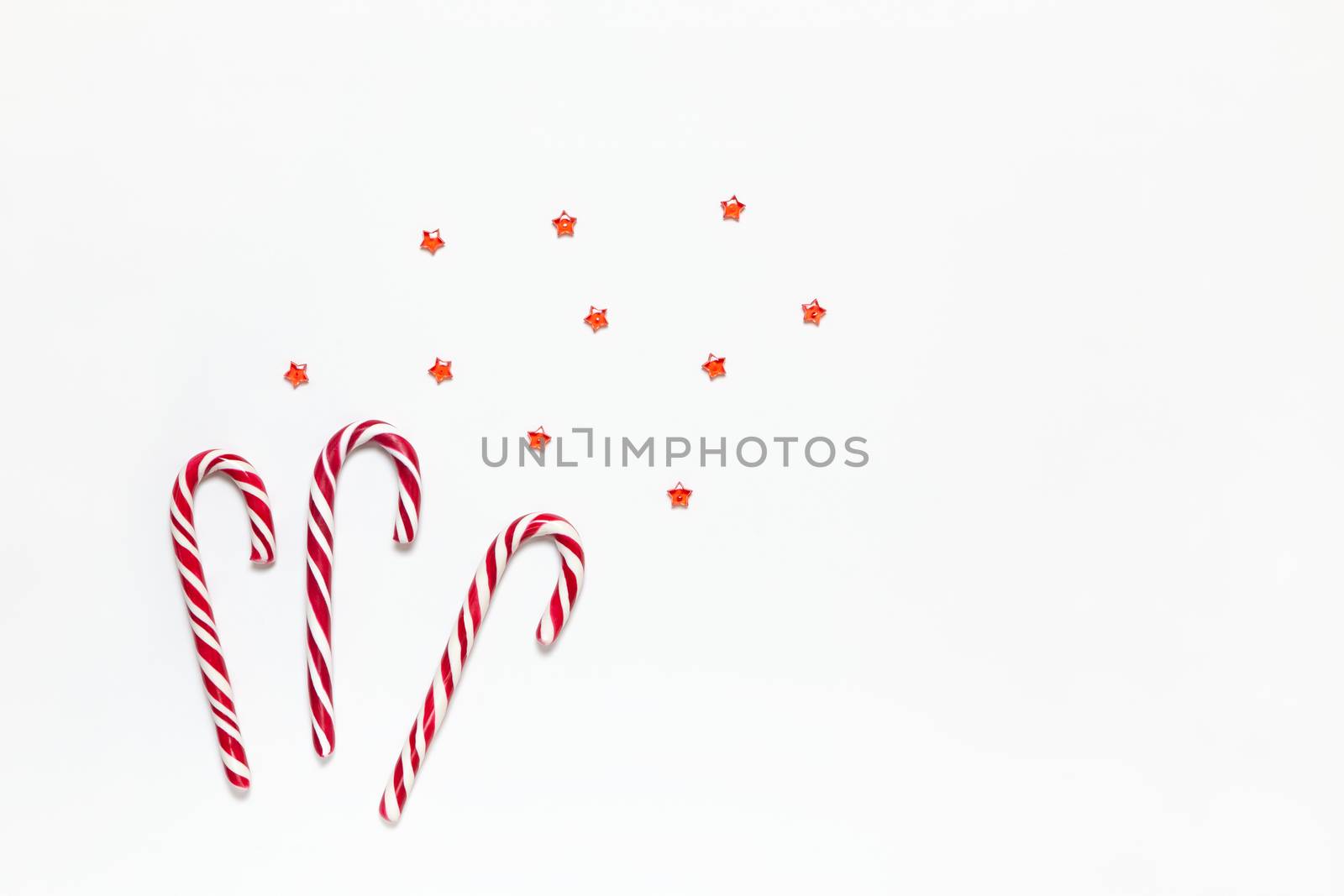 Christmas composition three caramel candy canes, confetti stars on white background with copy space. Festive minimal style flat lay. For greeting card, invitation. Horizontal.