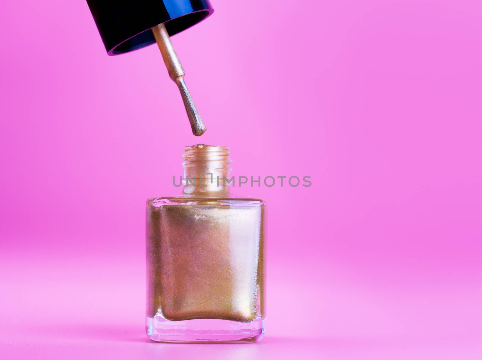 Opened bottle of gold nail polish, pink background