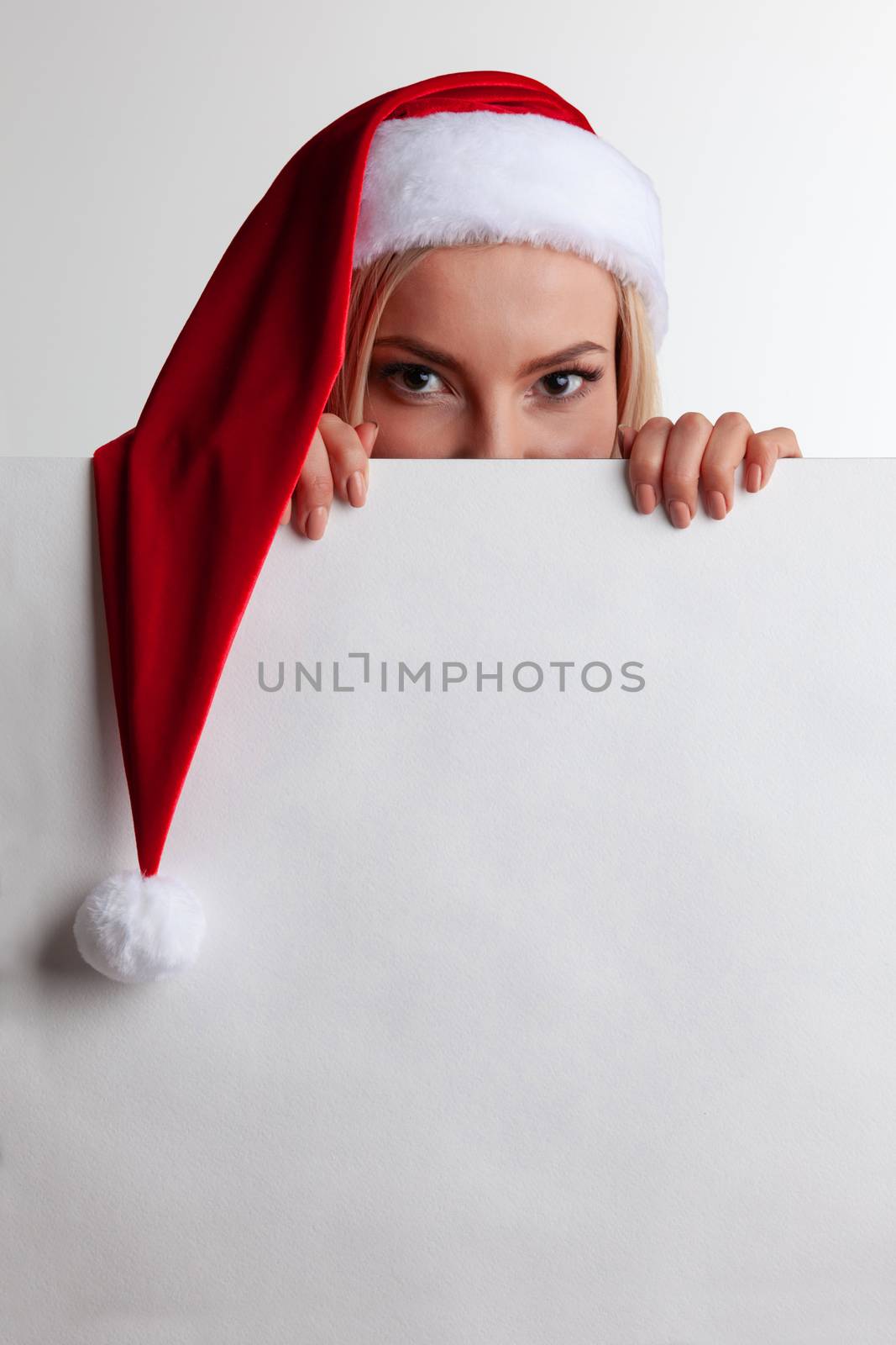 Santa girl hiding behind blank vintage sign billboard. Christmas woman in Santa hat showing paper sign.