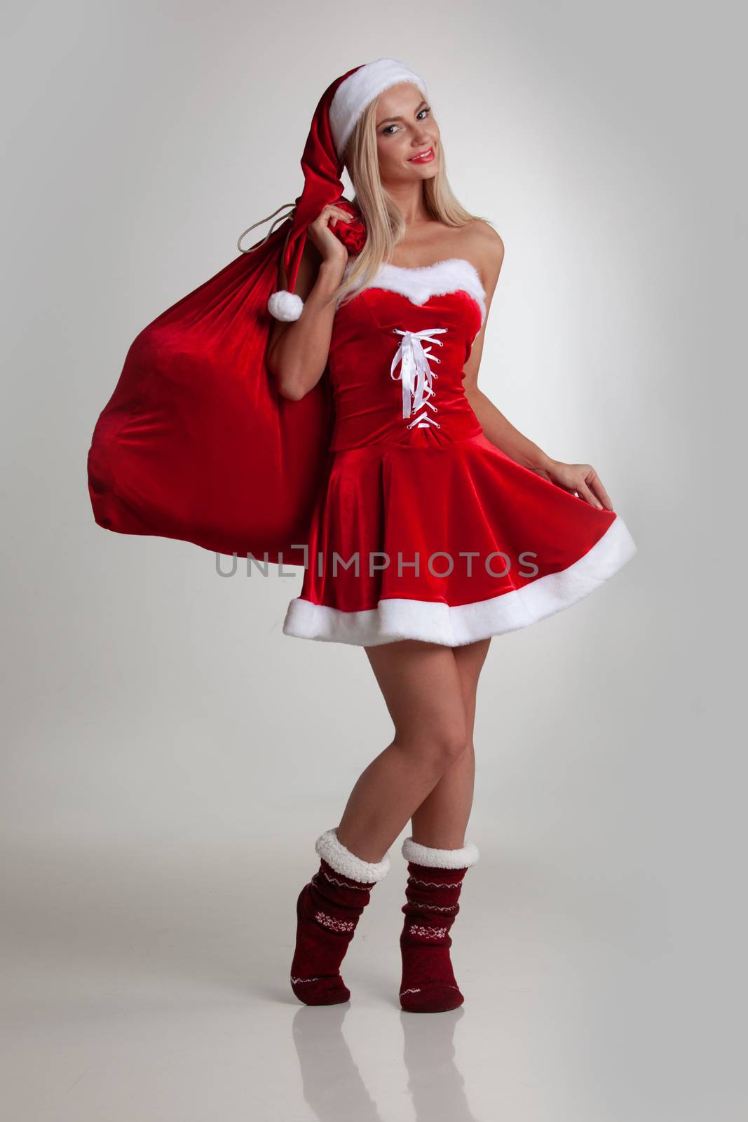 Cute young girl in santa claus dress and hat holding large gift bag on white background