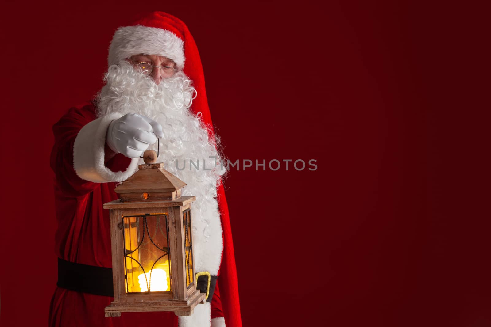 Photo of Santa Claus holding glowing lantern over dark red background with copy space for text