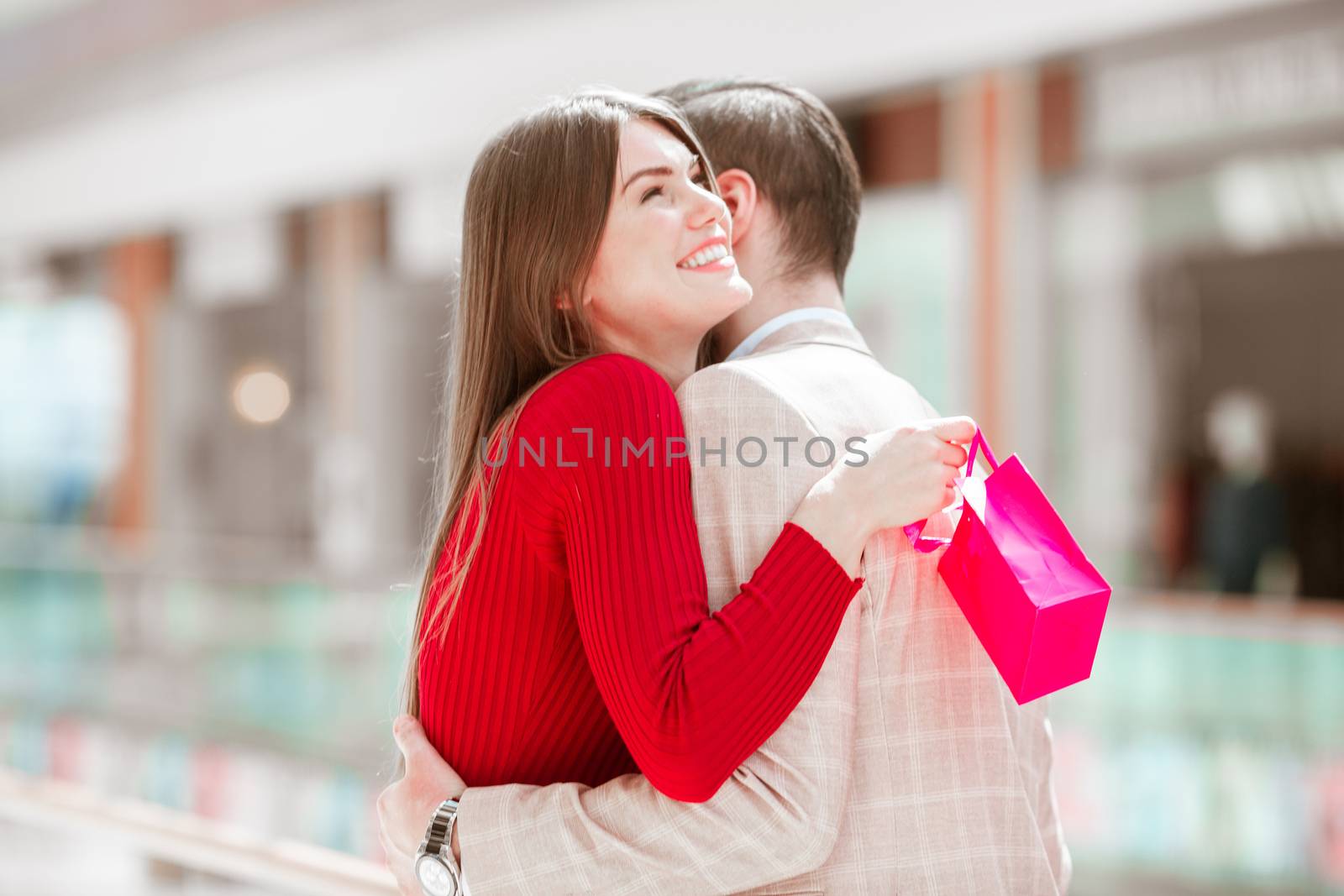 Beautiful young smiling grateful woman hugging man holding gift bag while shopping