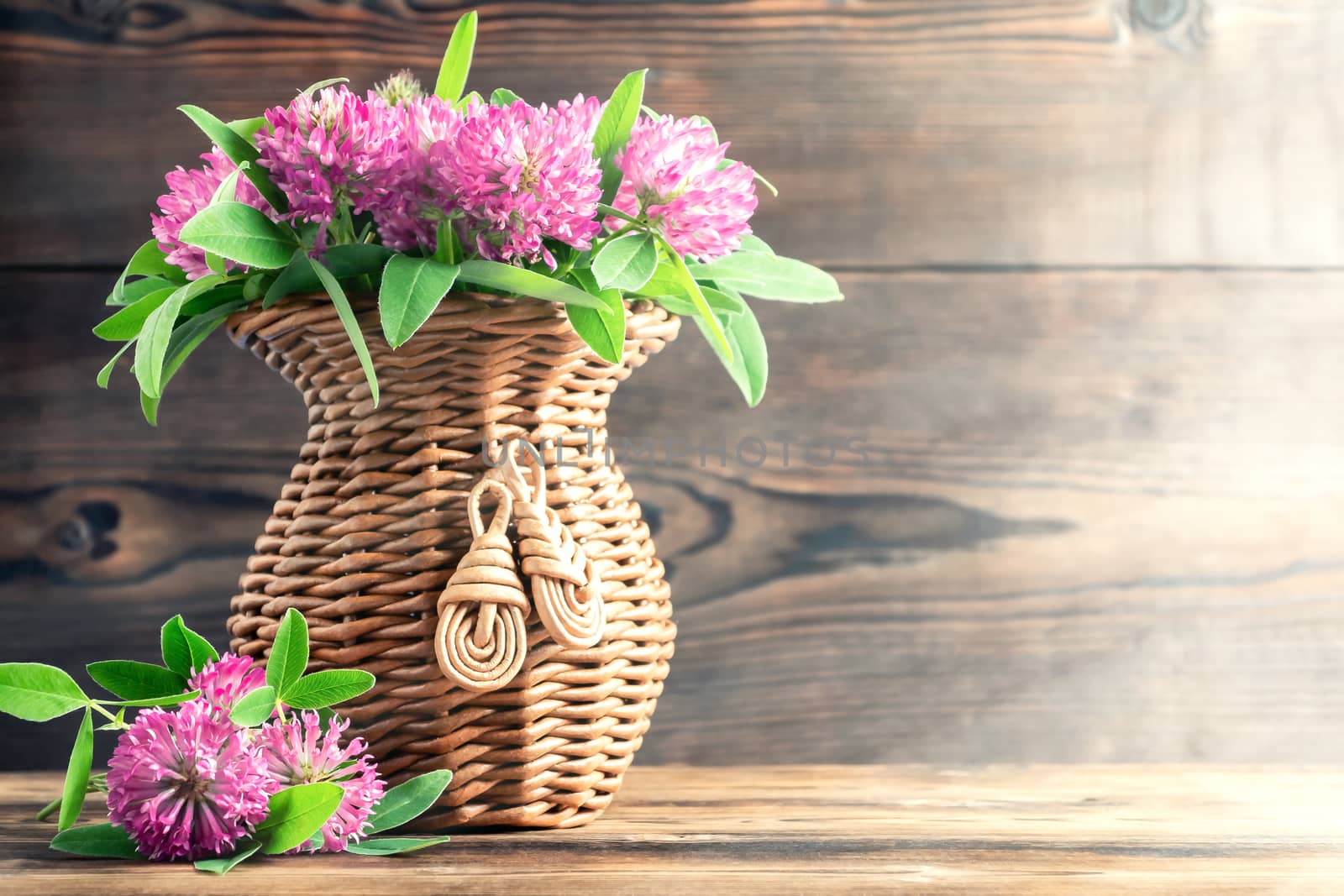 Bouquet of pink clover in a wicker vase on a wooden table on a summer morning by galsand