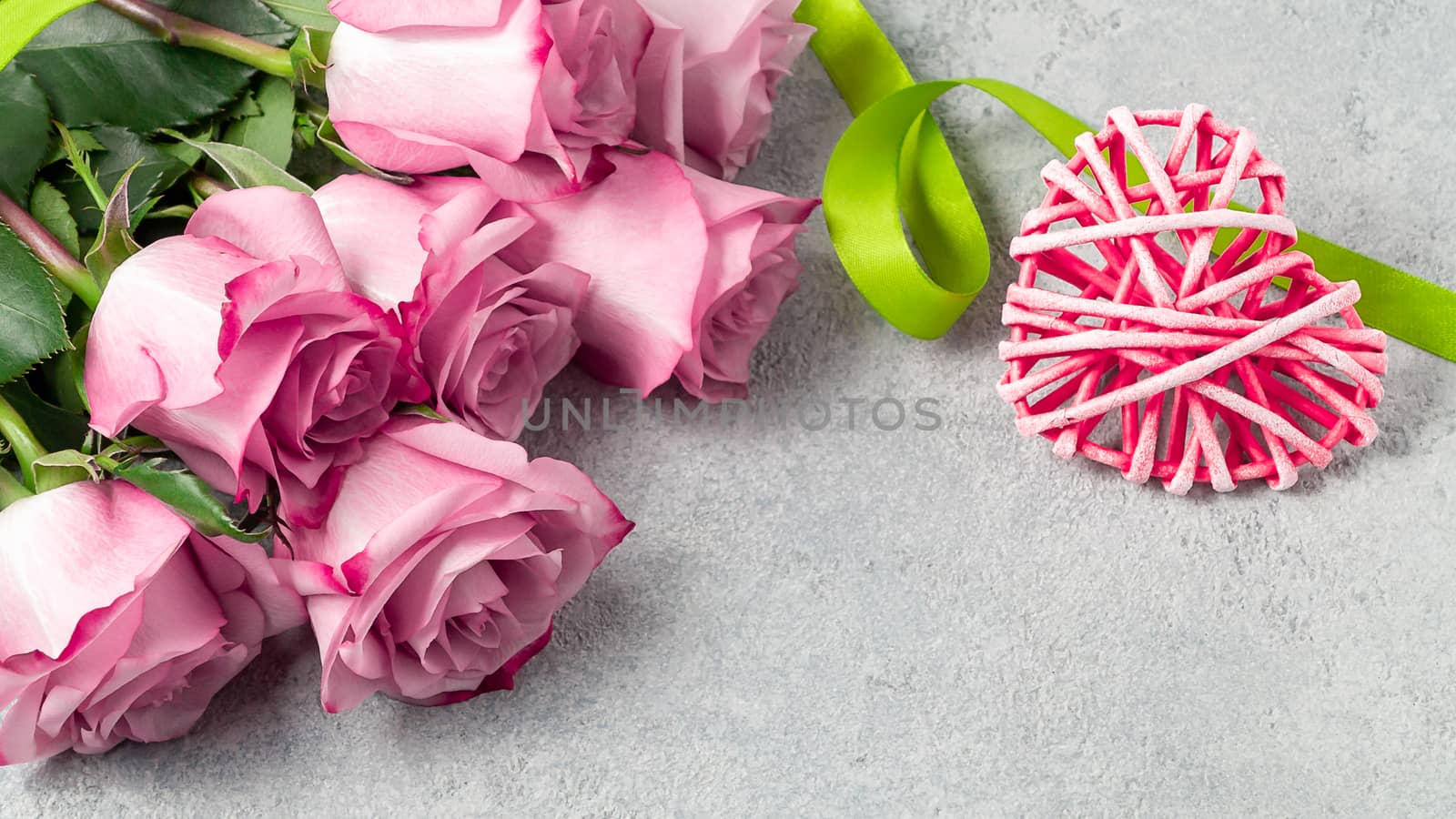 Flower arrangement - a bouquet of pink roses and wicker heart on a grey concrete surface, template for design or greeting card, place for text, copy space.