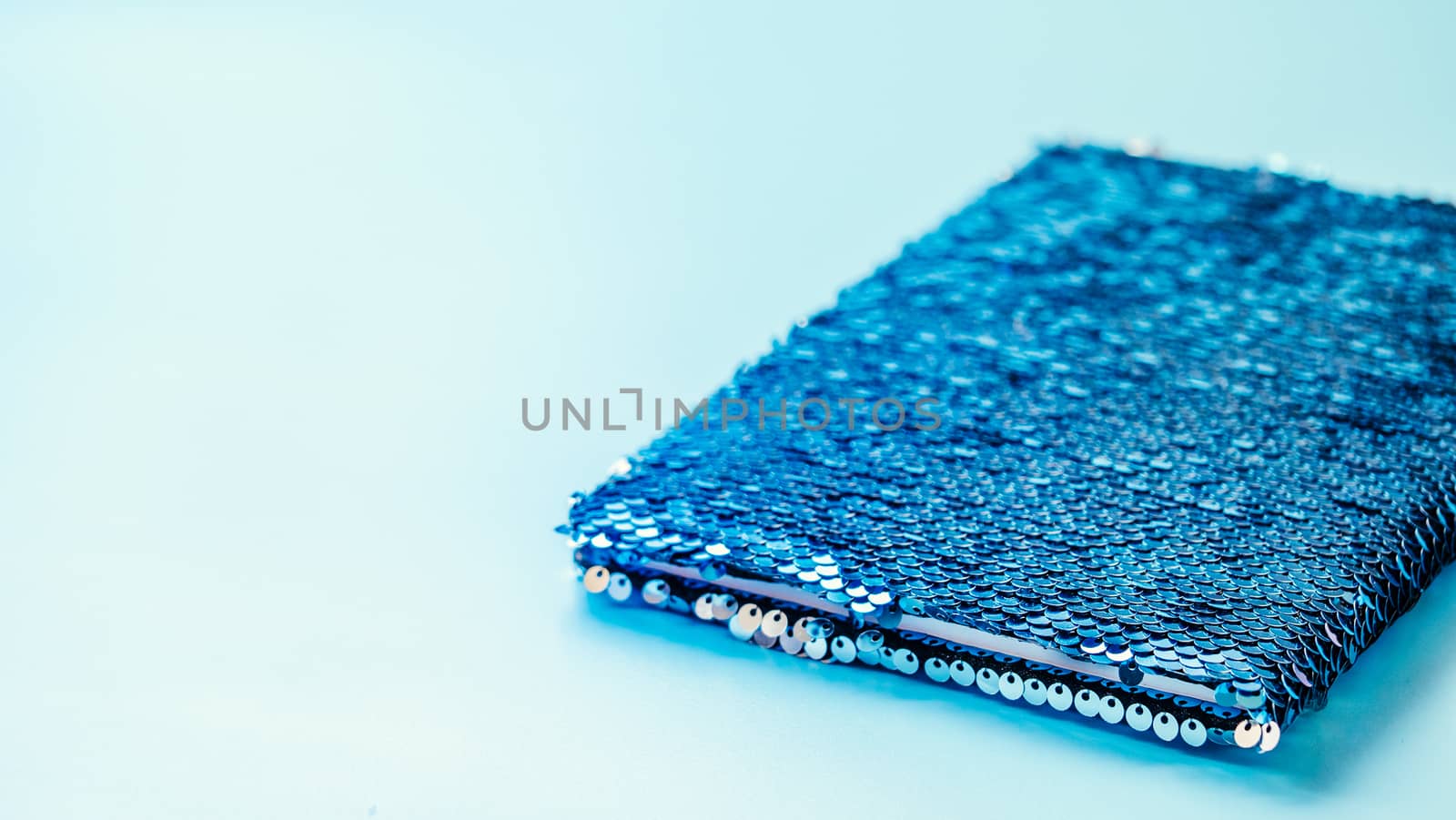 Anti-stress sequin surface notebook on blue background. Trendy sequin notepad with copy space left. Horizontal banner. Negative space for text or design.