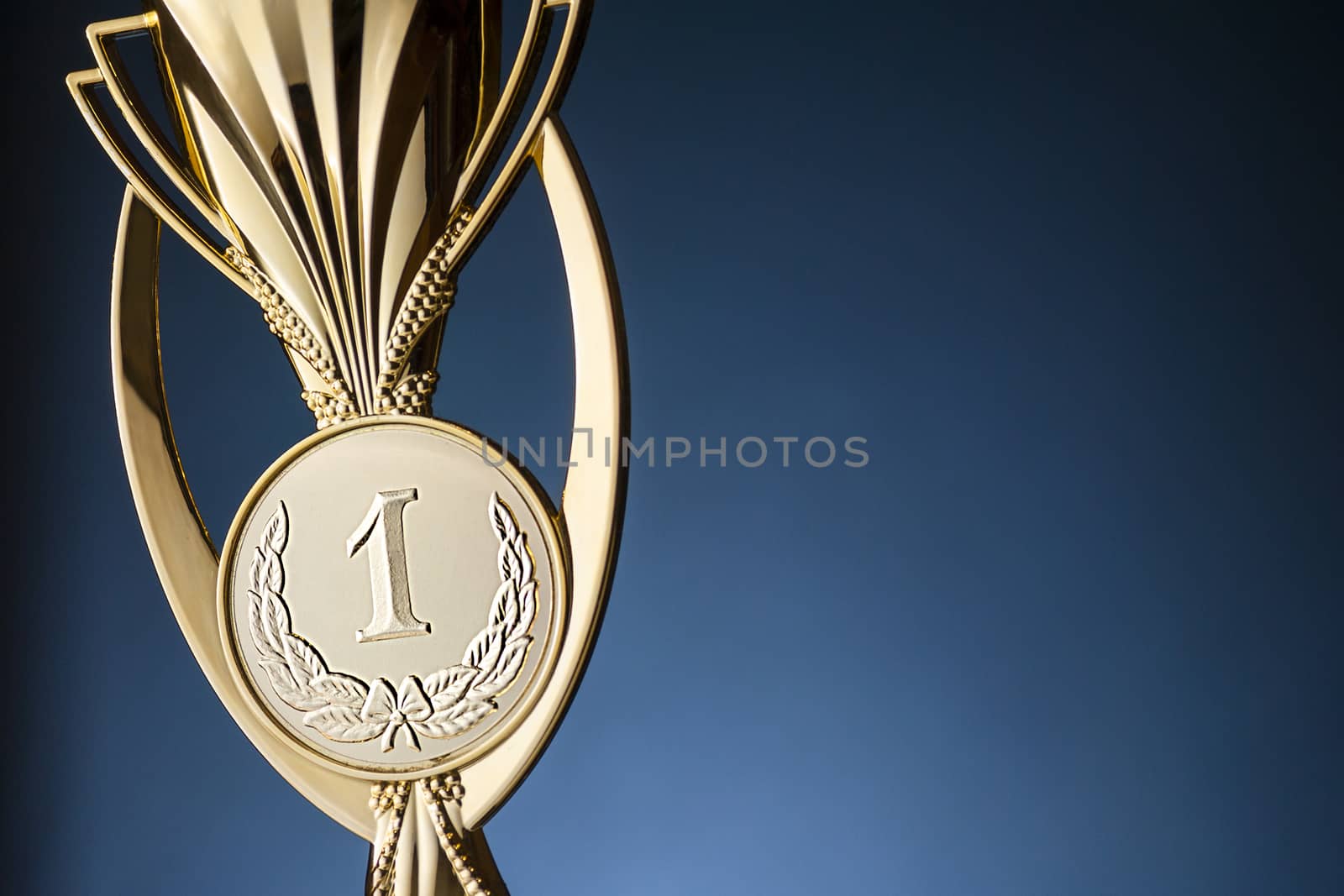 Gold championship winners trophy or cup placed to the side on a blue background with copy space