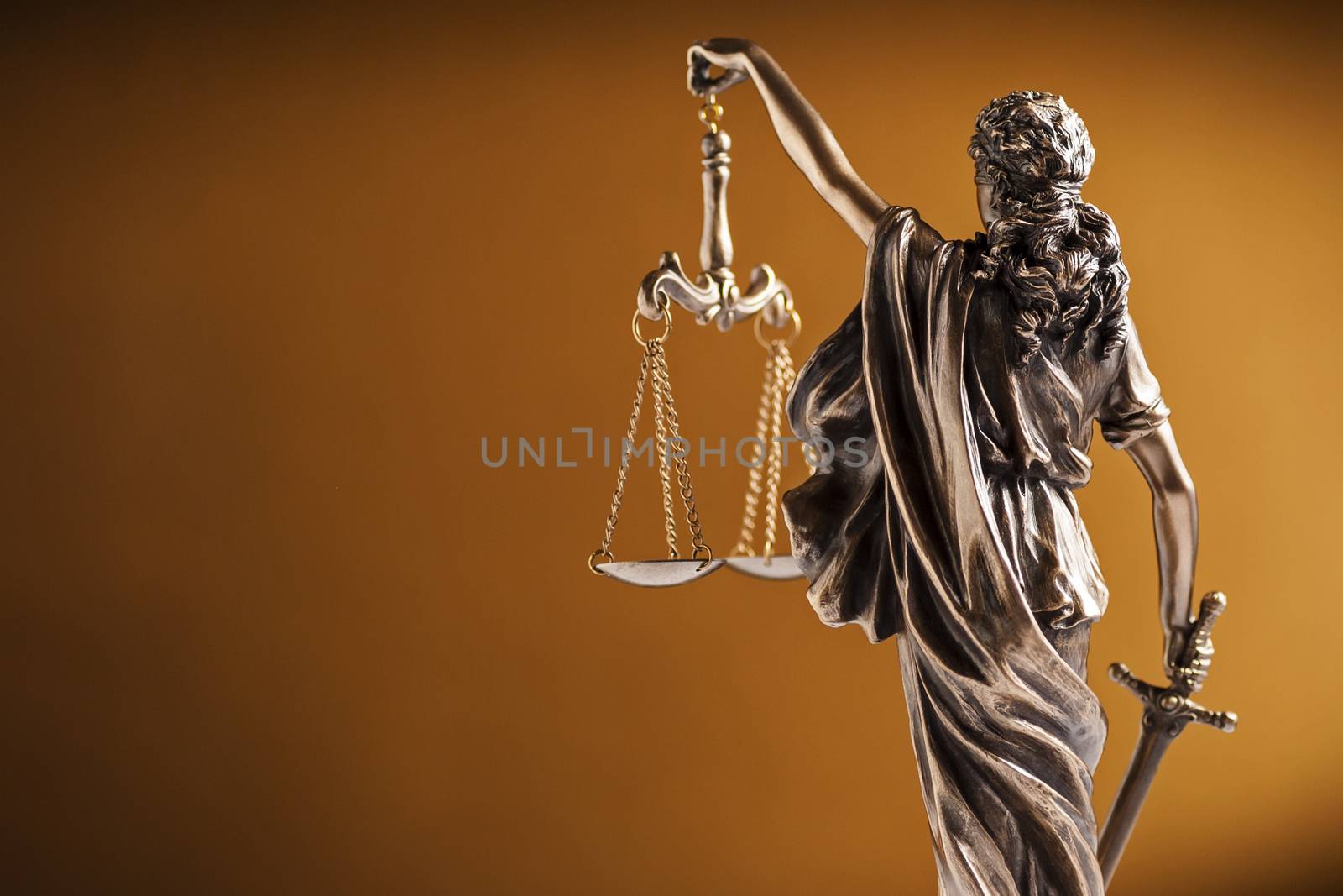Rear view of a small statue of Lady Justice holding up the scales of law and order and carrying a sword over a graduated brown background with copy space