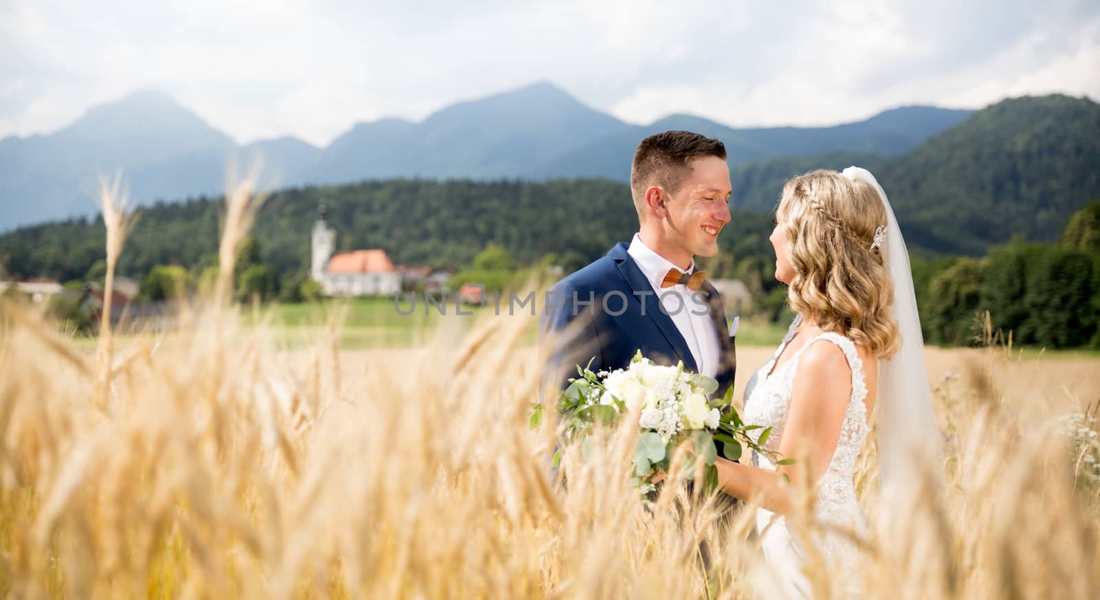 Groom hugs bride tenderly in wheat field somewhere in Slovenian countryside. by kasto