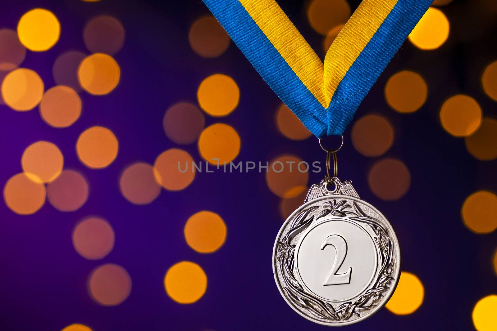 Silver second place runner up championship medallion on a ribbon hanging over a blue background with colorful orange bokeh effect of party lights