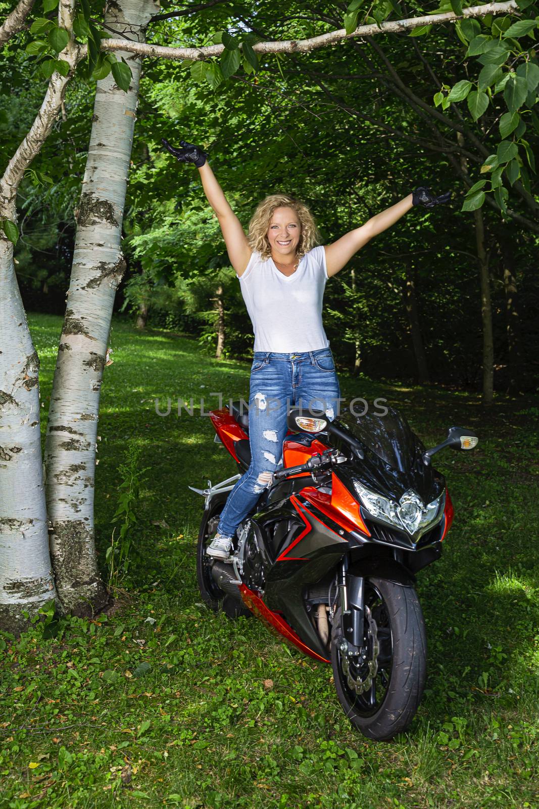 Young woman standing up on her motocycle with her hands in the air