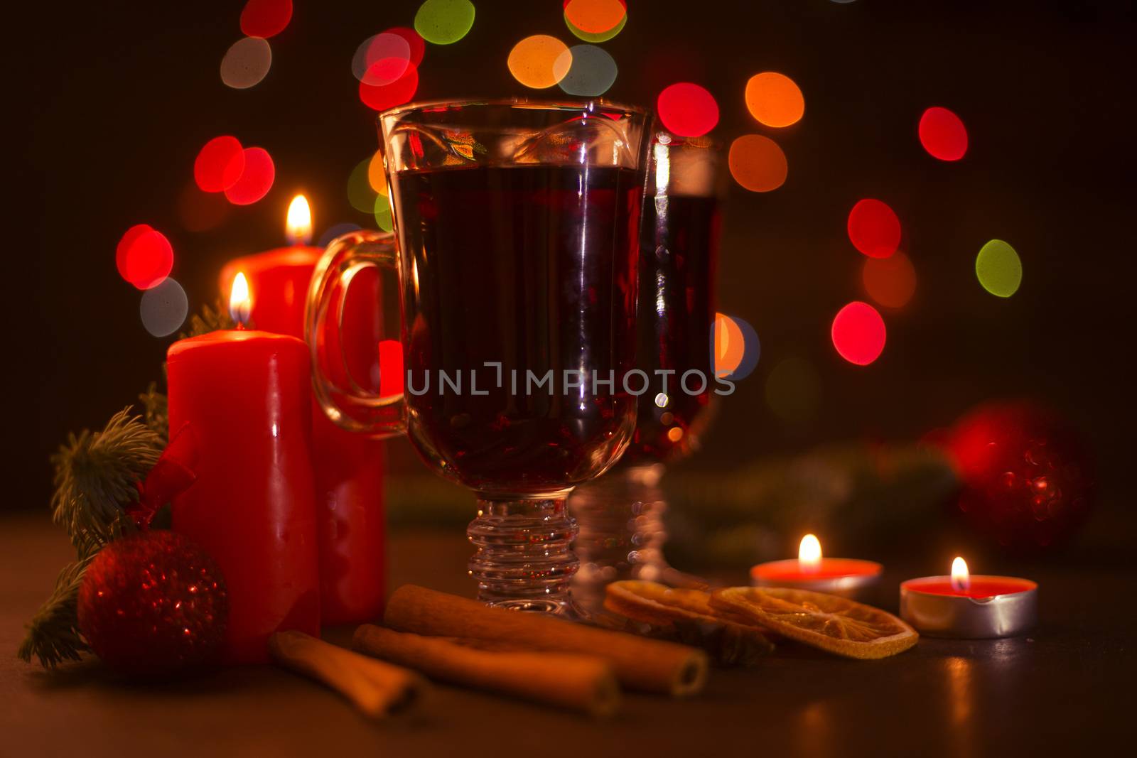 Mulled wine with cinnamon sticks orange candles fir tree branch and baubles over holiday christmas lights background