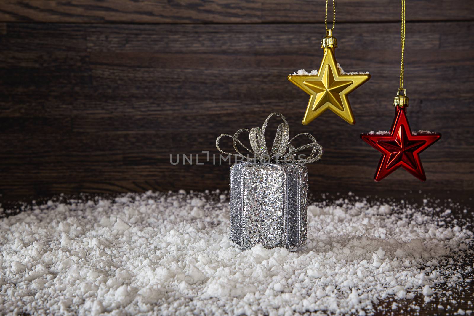 Silver present, in the snow, with gold and red star hanging over head on the dark wood background