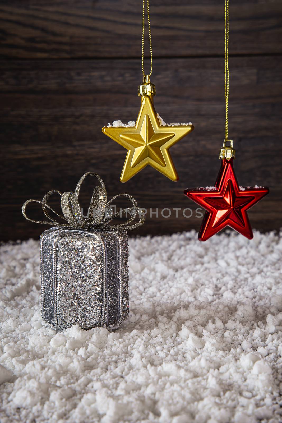 shiny silver present with red and gold star, in the snow in front of a wood background