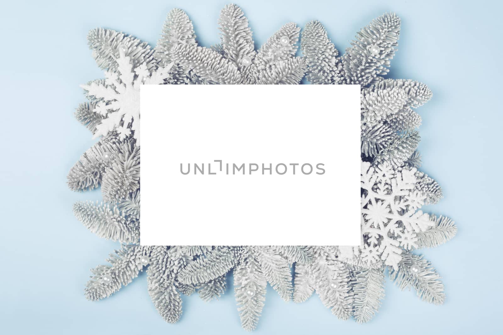 Frosted fir tree twigs and Christmas decorative bauble balls on blue background with white rectangle card with copy space for text template flat lay top view design