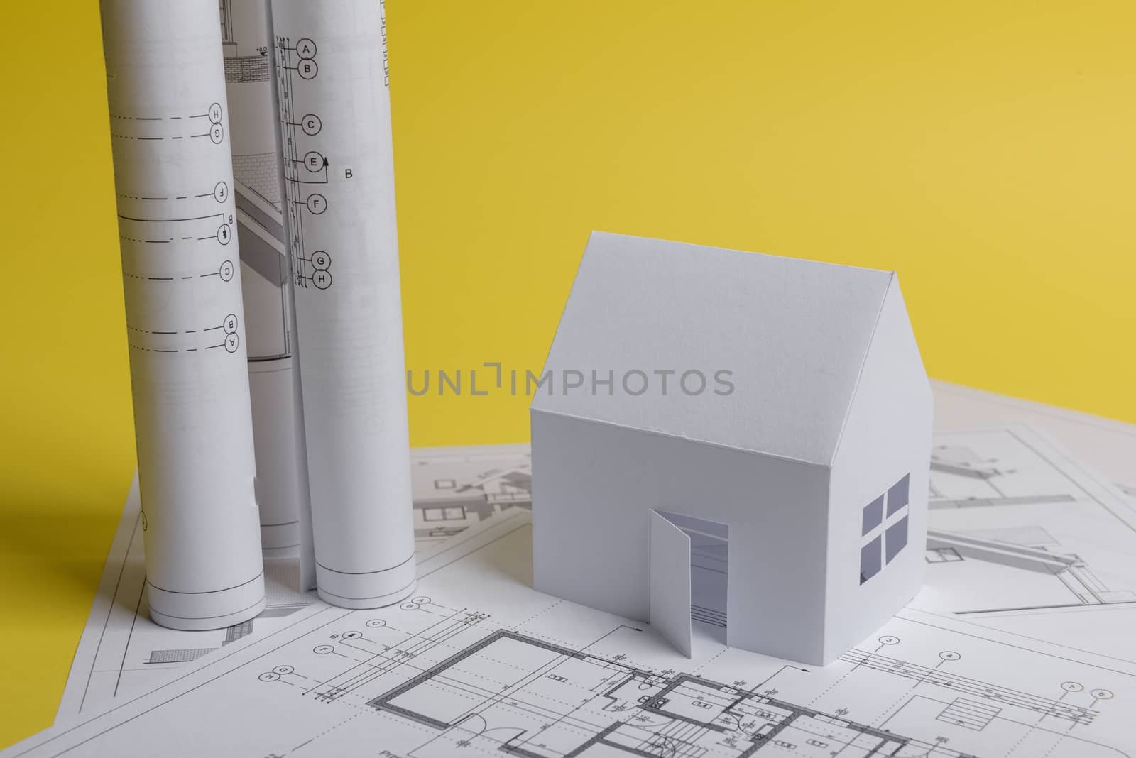 White family paper house, house projects plan and blueprints in the background. Minimalistic and simple concept, style. Horizontal orientation. View from above.