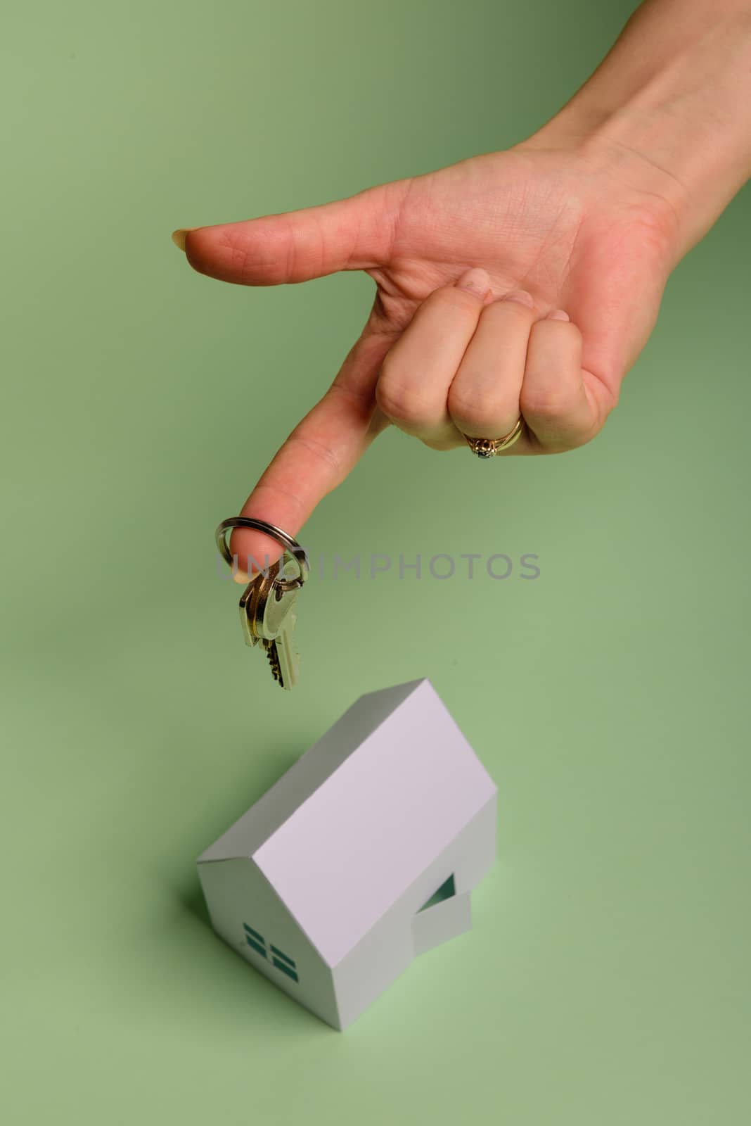 White family paper house. House keys in hand on mint background paper. Minimalistic and simple concept, style. Copy space. Vertical orientation. Family moving or removal concept.
