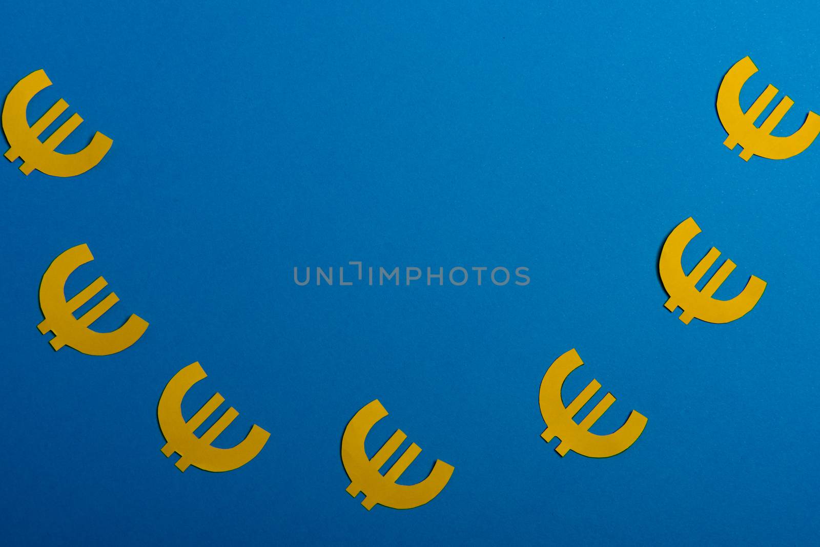 Paper yellow symbols of euro currency on blue background. View from above with copy space