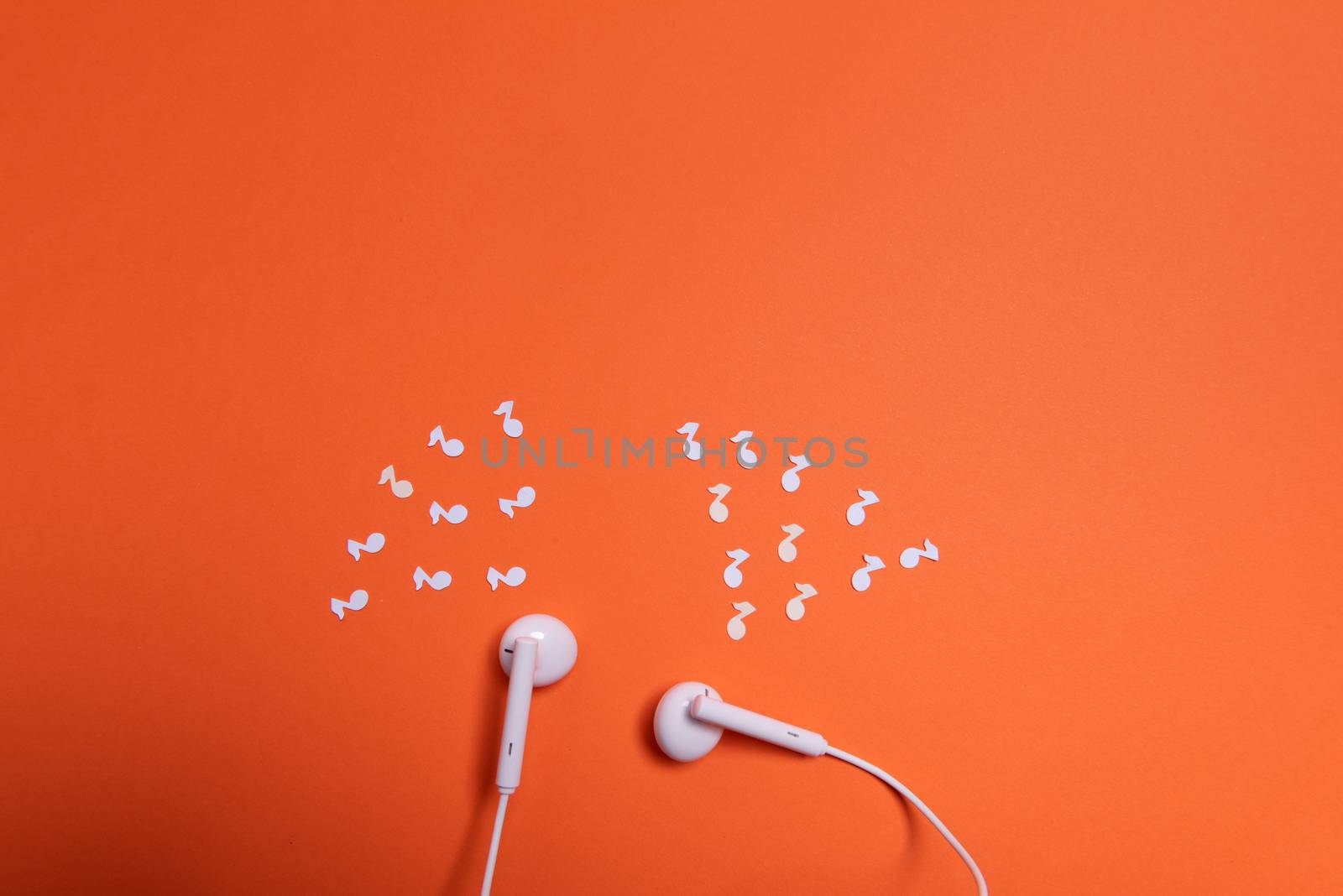 white earphones and white paper notes on orange background. view from above