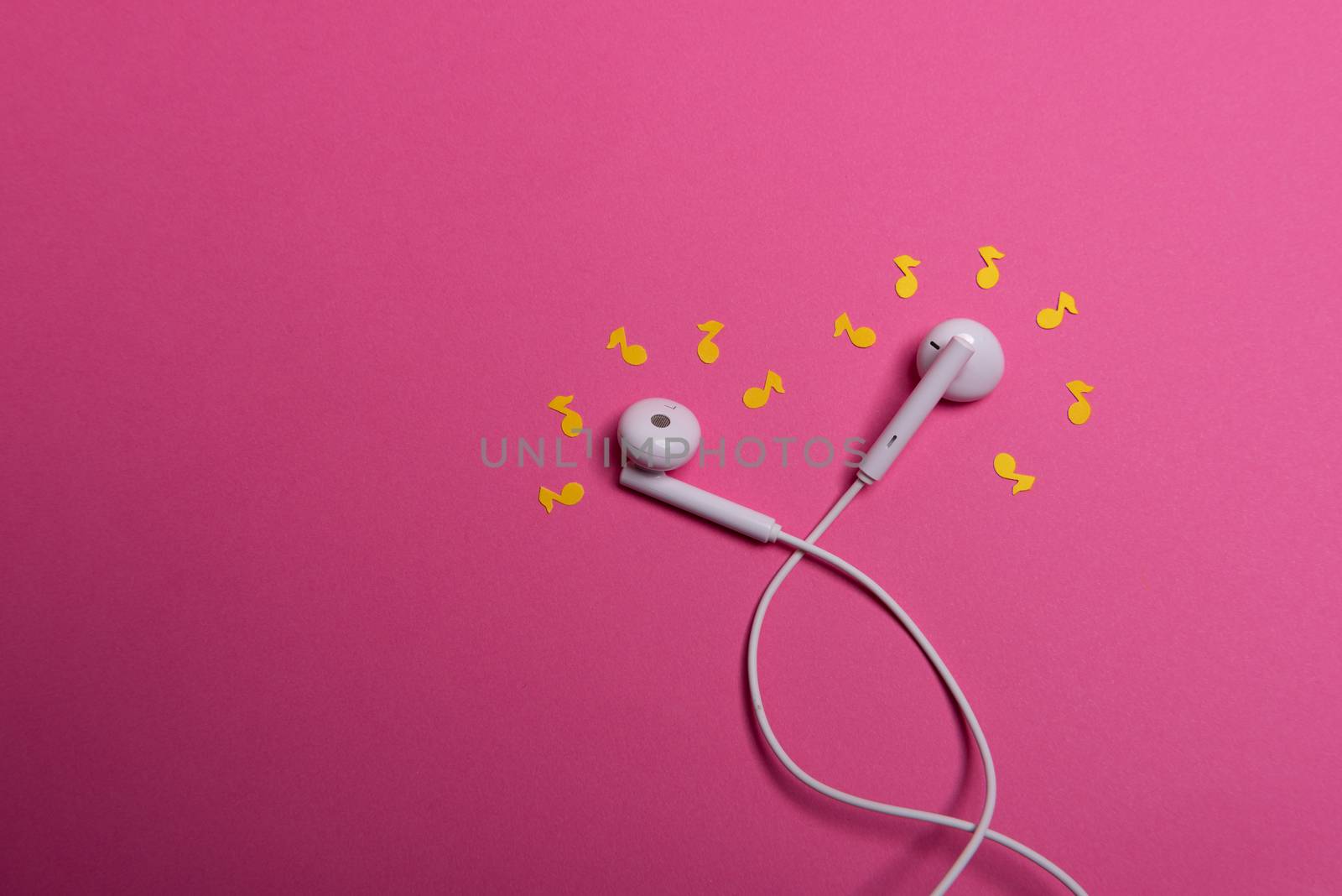 white earphones and yellow paper notes on pink background. view from above