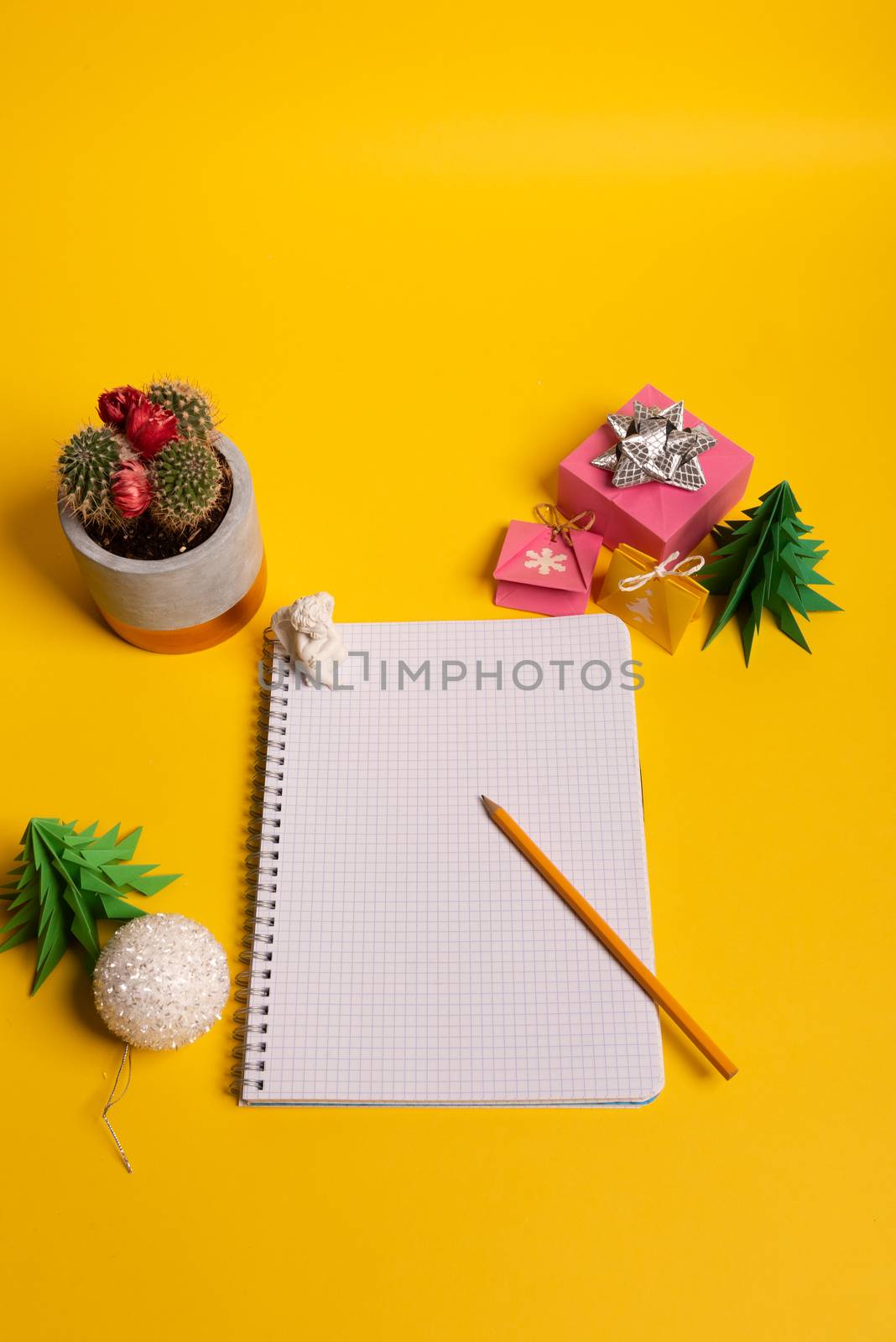 gift box and green origami trees with notepad on yellow desk, table