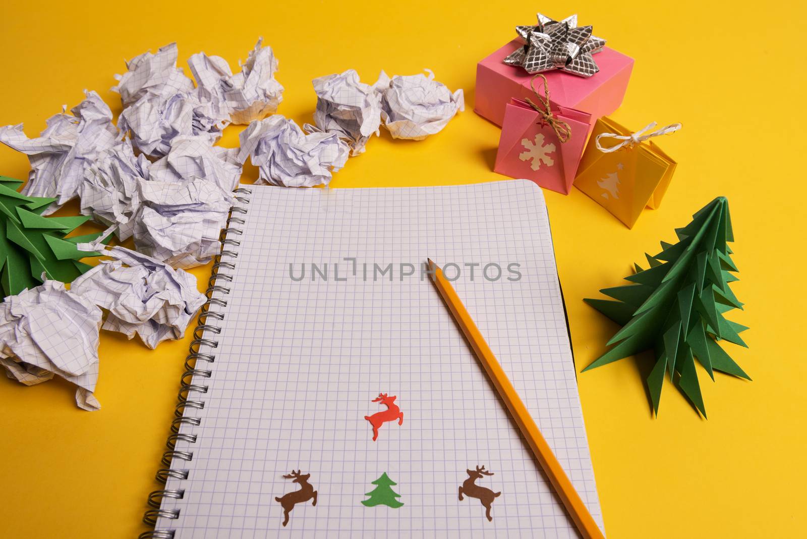 gift box and green origami trees with notepad on yellow desk, table