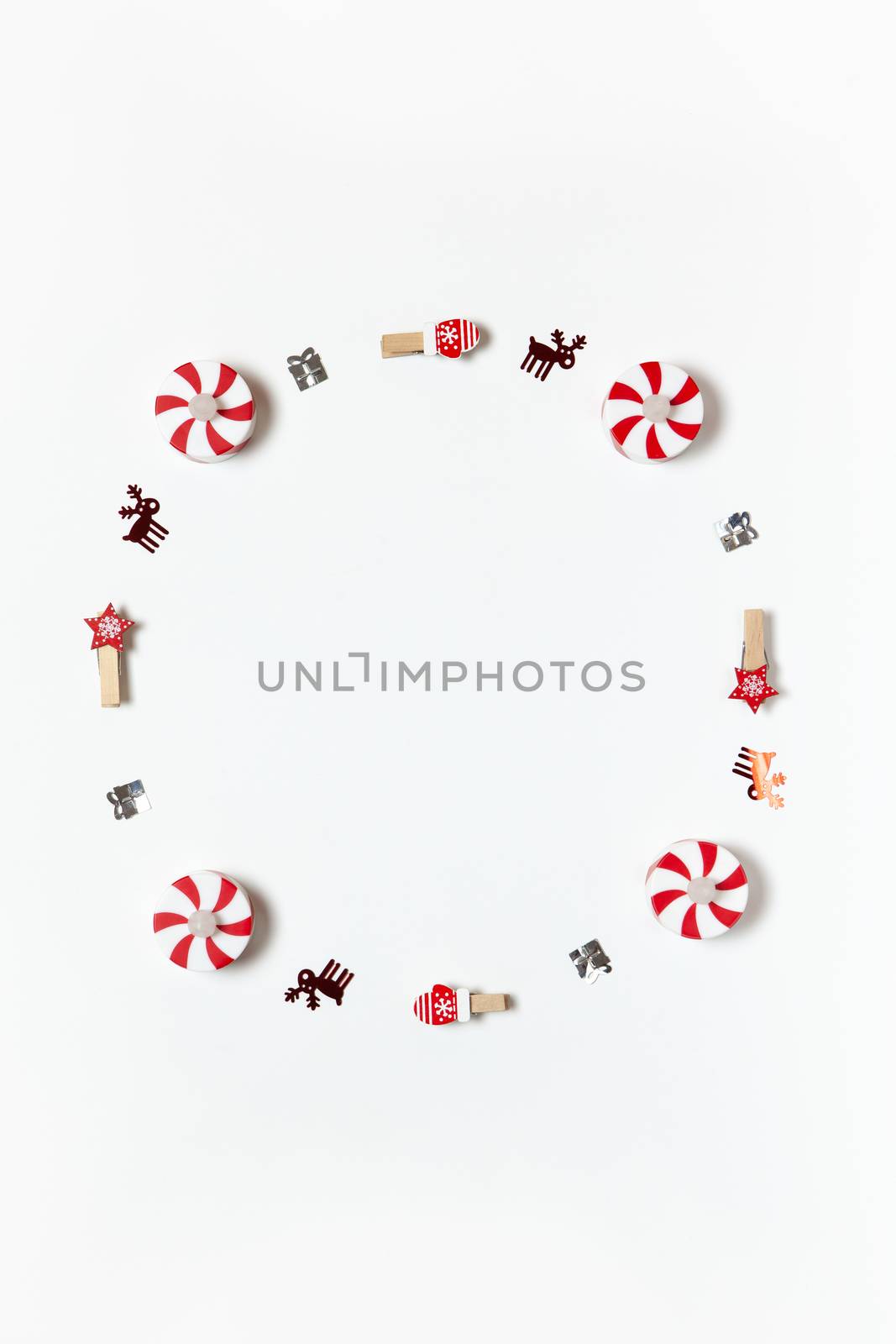 Simple Christmas composition. Round frame of clothespins, candy-bulbs, deer confetti and gifts on white background, copy space. Vertical. Minimal style. Top view. For social media, greeting card.