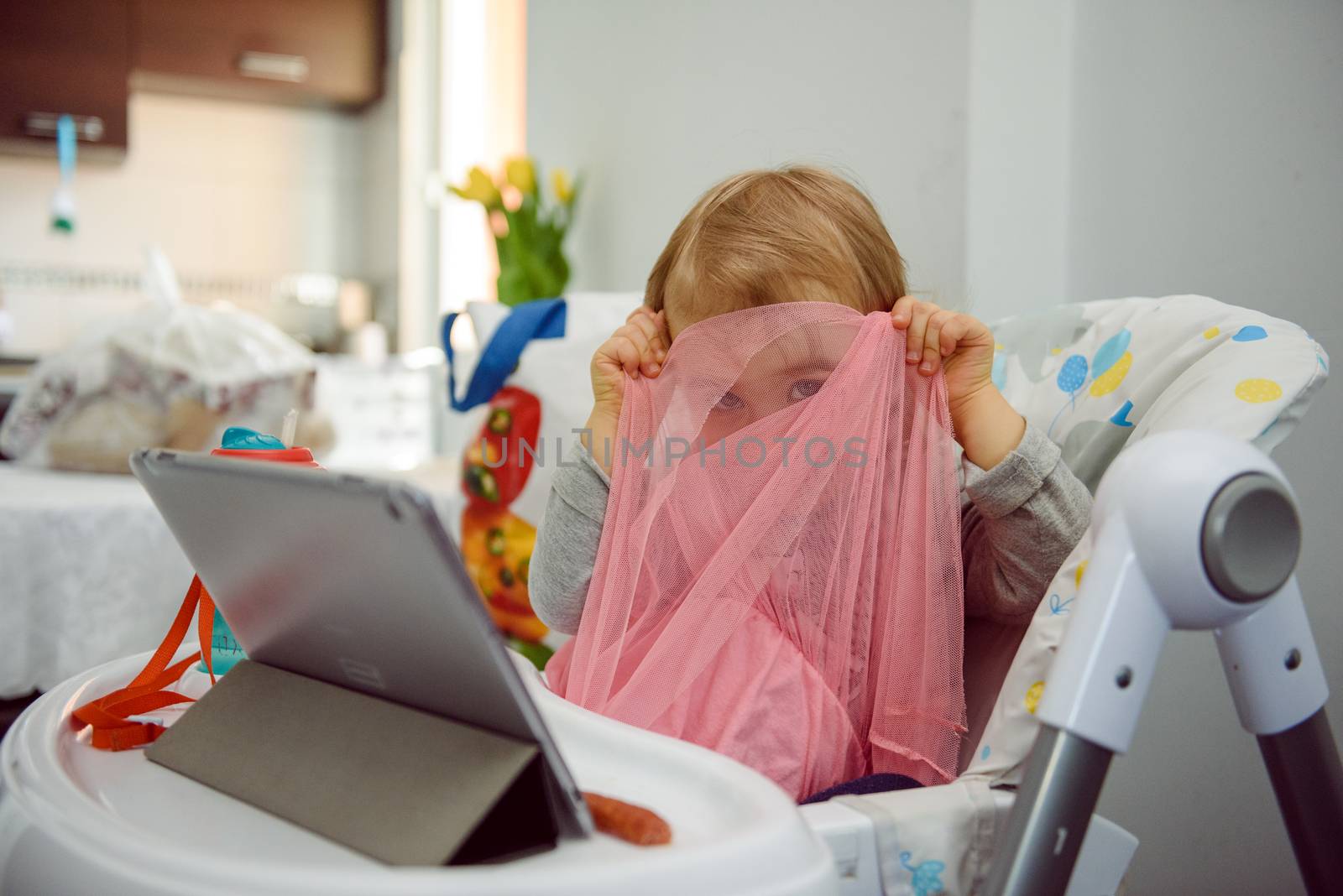 cute blond child sits in a children's chair at the kitchen and eat a juicy peach. Little girl with a piercing look.