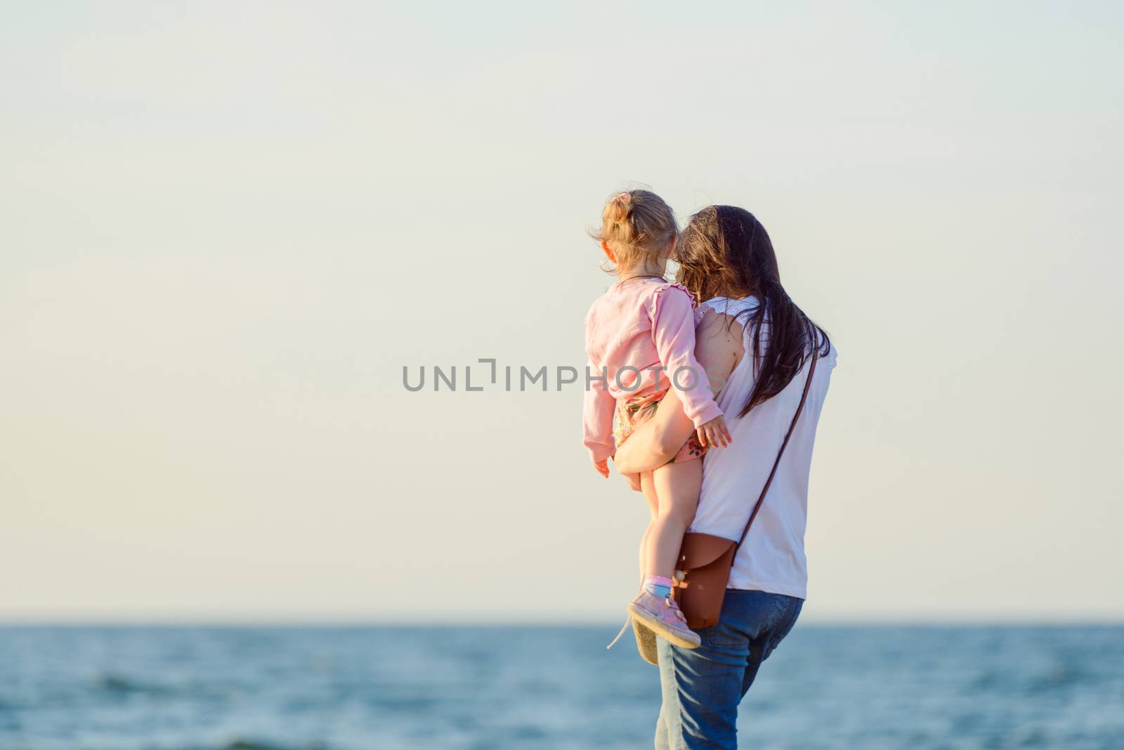 Mother and little daughter walking on the beach.