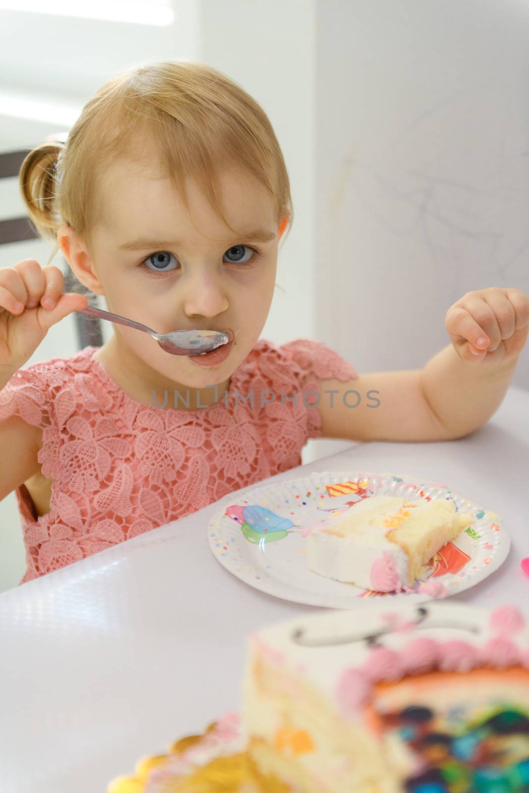 Baby girl 1 year old eating birthday cake in room. Birthday party. Childhood.