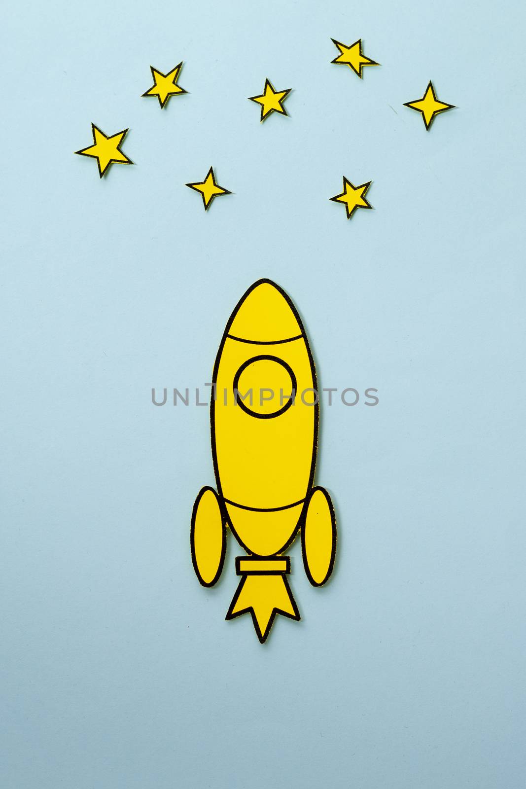 Yellow cartoon rocket flying through space towards the stars in a concept of success and achievement over a blue background with copy space